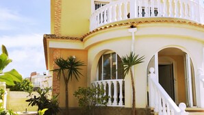 A two-story building with a white balcony, potted plants, and a staircase leading to the entrance.