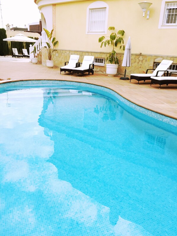 A swimming pool with lounge chairs and potted plants.