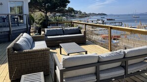 Eine Terrasse mit Korbmöbeln, einem Tisch und Blick auf das Meer und Boote.