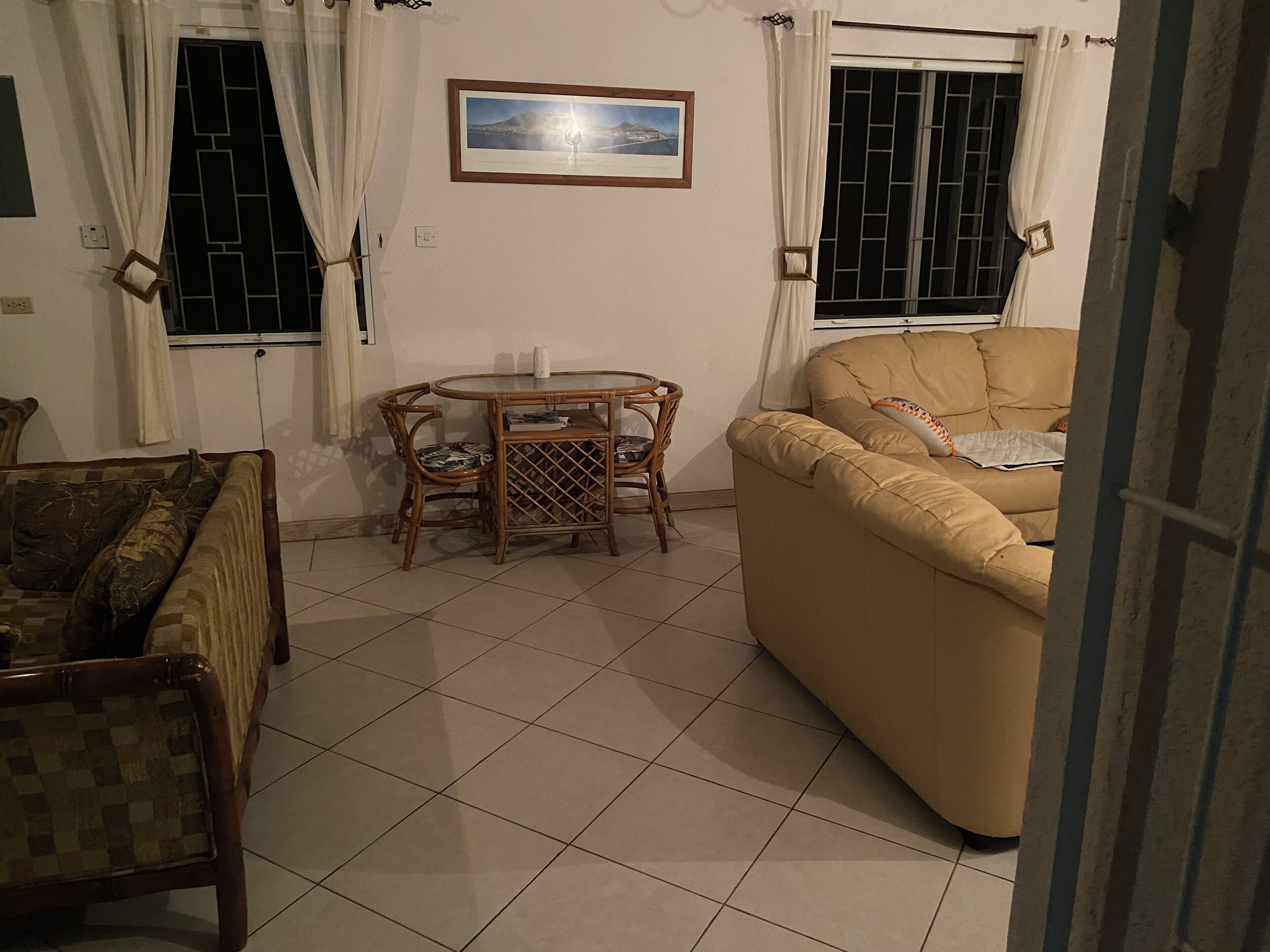Un saló amb un sofà beix, una taula de dinar amb cadires, i una finestra amb cortines.