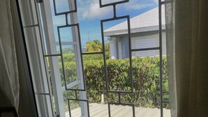 A view through a window with a metal grid, a white curtain, and a glimpse of a building and greenery outside. - Villa, 4 beds, 3 bathrooms, 1 minute to beach by car or 10 minute stroll (Westmoreland)