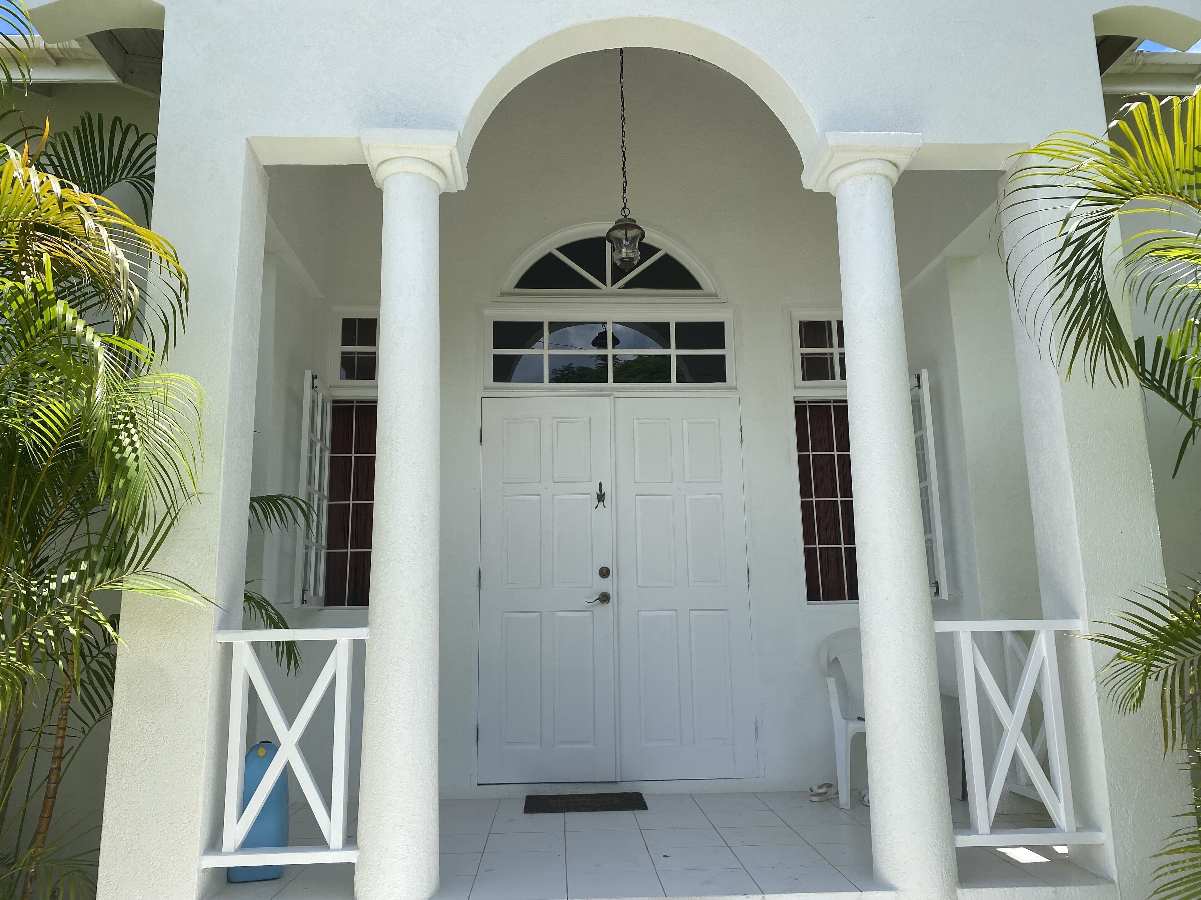 A white building with a central door, two windows on either side, and a small balcony with a chair.