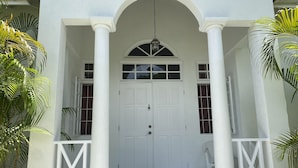 A white building with a central door, two windows on either side, and a small balcony with a chair. - Villa, 4 beds, 3 bathrooms, 1 minute to beach by car or 10 minute stroll (Westmoreland)