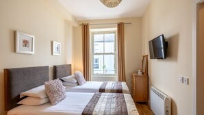 A hotel room with two beds, a television, a dresser, and a window with curtains. - A 2 bed apartment that sleeps 4 guests  in 2 bedrooms (kenmare)