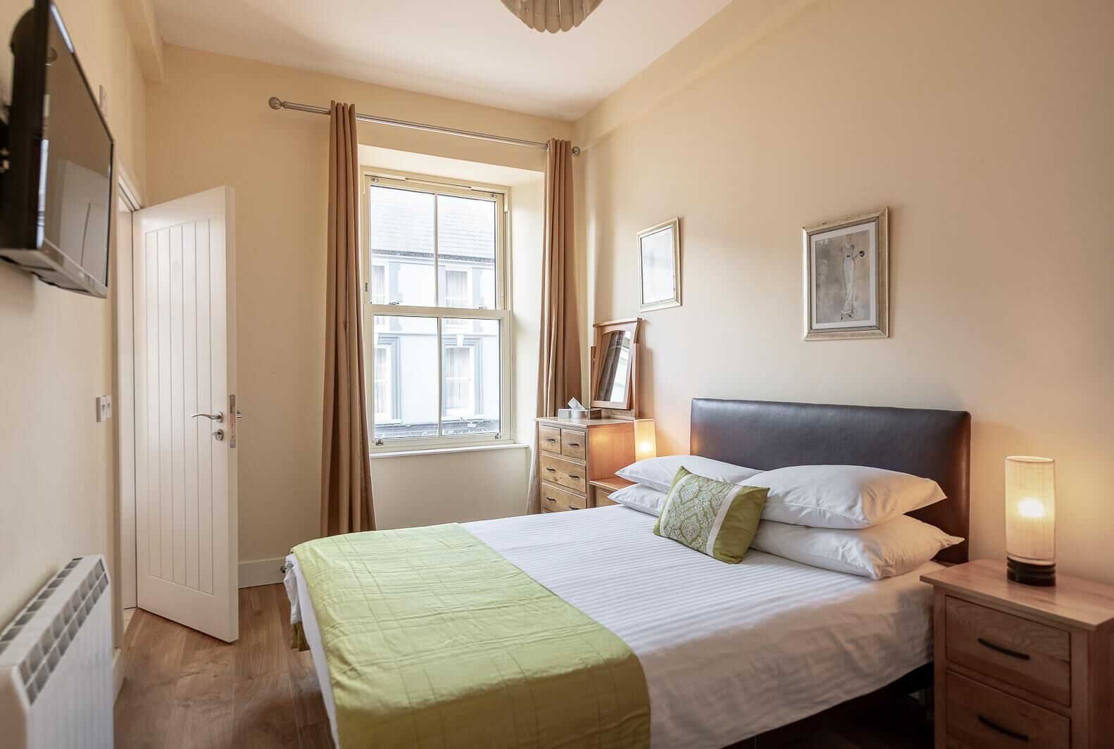 Ein Hotelzimmer mit Bett, Nachttisch, Lampe, Fenster und Tür.