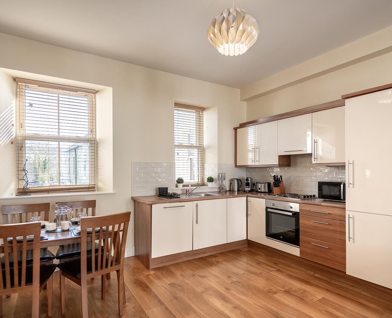 A modern kitchen with wooden cabinets, a dining table with chairs, and a large window with blinds.