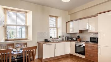A modern kitchen with wooden cabinets, a dining table with chairs, and a large window with blinds.
