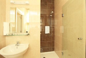Bathroom features a pedestal sink, glass shelf, and a shower area with handheld showerhead.