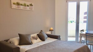 A bedroom with a bed, a nightstand, a lamp, a dining table, and a view of the outside. - Modern and bright, a stone's throw from the sea (Quartu Sant'Elena)