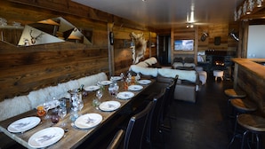 Ein Holzinterieur mit einem langen Esstisch, der für eine Mahlzeit gedeckt ist, einem Kamin und einer Bar.