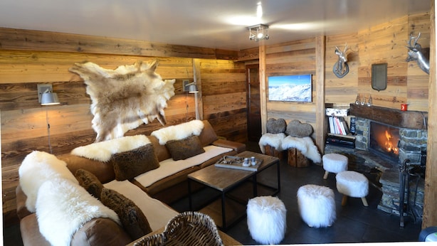 Ein gemütliches Blockhaus-Interieur mit Kamin, bequemen Möbeln und einem aufgehängten Tierkopf.