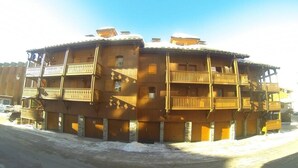Ein mehrstöckiges Holzhaus mit Balkonen, verschneitem Gelände und blauem Himmel.