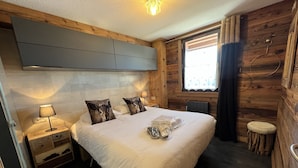 Ein gemütliches Schlafzimmer mit einem großen Bett, Holzwänden, einem Fenster mit Vorhängen und einem Nachttisch mit Lampe.