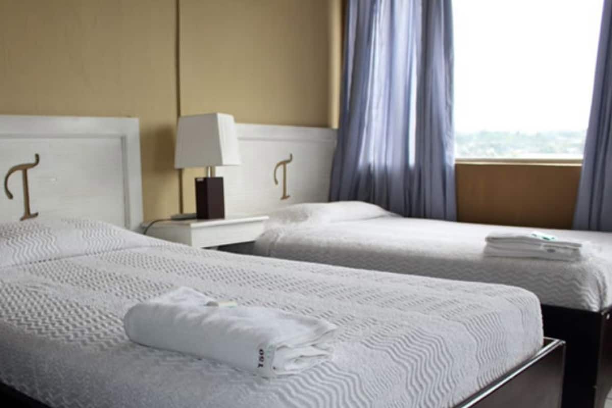 A hotel room with two beds, each with a white headboard and a lamp on the nightstand.