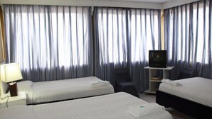 Une chambre d’hôtel avec deux lits, un téléviseur posé sur un meuble, une chaise et une lampe.