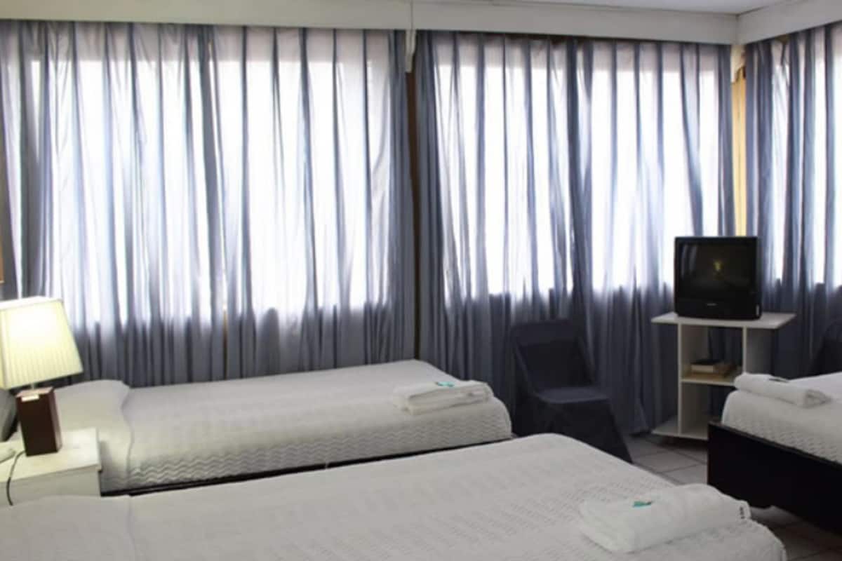 A hotel room with two beds, a TV on a stand, a chair, and a lamp.