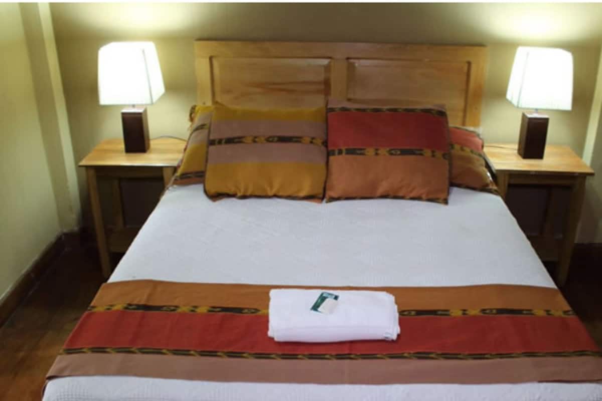 A neatly made bed with a brown and red patterned bedspread, two bedside lamps, and a folded white towel on the bed.