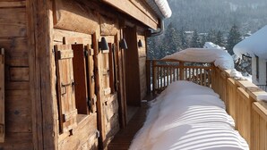 Eine Holzhütte mit einer mit Schnee bedeckten Terrasse und Blick auf verschneite Bäume im Hintergrund.