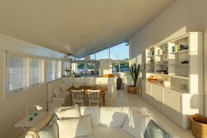 Ein geräumiger Wohnbereich mit einem großen weißen Sofa, einem Esstisch und einer Küchenzeile mit weißen Schränken und Regalen.