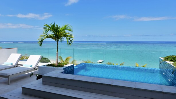 Una piscina en la azotea con agua azul cristalina, sillas de descanso blancas y vistas al océano.