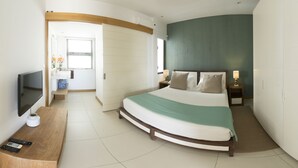 Habitación de hotel moderna con una cama curvada, un televisor de pantalla plana, un escritorio de madera y un baño visible a través de una puerta abierta.