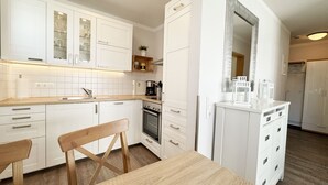 Moderni keittiö, jossa on valkoiset kaapit, puinen ruokapöytä ja sisäänrakennettu uuni.