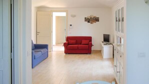 Una sala de estar con un sofá rojo, un sillón azul y un mueble blanco con un televisor.