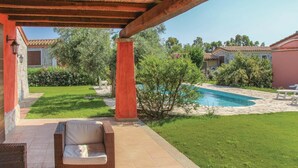 Un patio techado con mobiliario de mimbre, piscina y jardín bien cuidado.