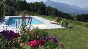 Ein Schwimmbad mit Bergblick, umgeben von einem Garten mit verschiedenen Blumen.