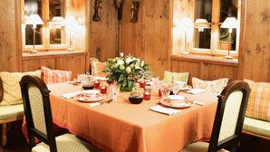 Ein Esszimmer mit Holzvertäfelung, einem für vier Personen gedeckten Tisch und zwei Fenstern mit Lampen.