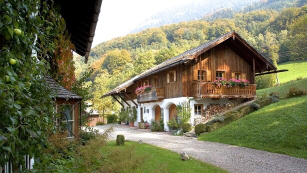 Eine Holzchalet mit einem Balkon, umgeben von üppiger Vegetation und einer Berglandschaft im Hintergrund.