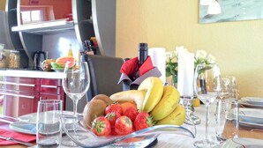 Una mesa de comedor dispuesta con frutas, copas de vino y un florero con flores.