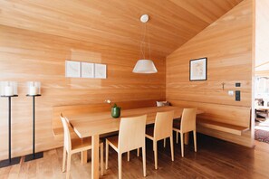 Een houten interieur met een lange eettafel, stoelen, een hanglamp en lijstwerken aan de muren.