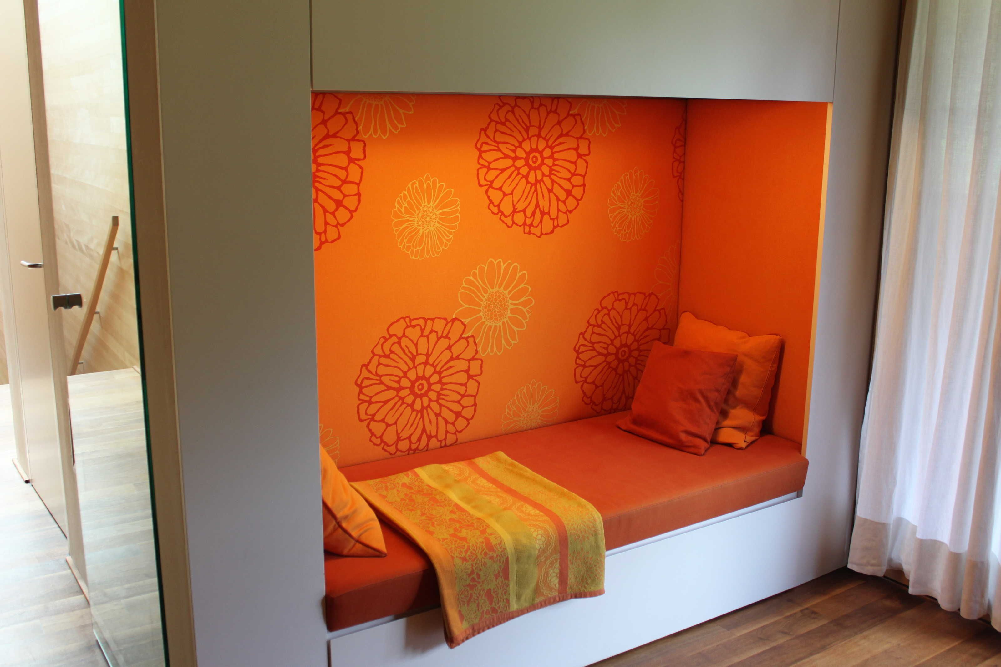 A room with a built-in seating area featuring orange cushions and a patterned wall.