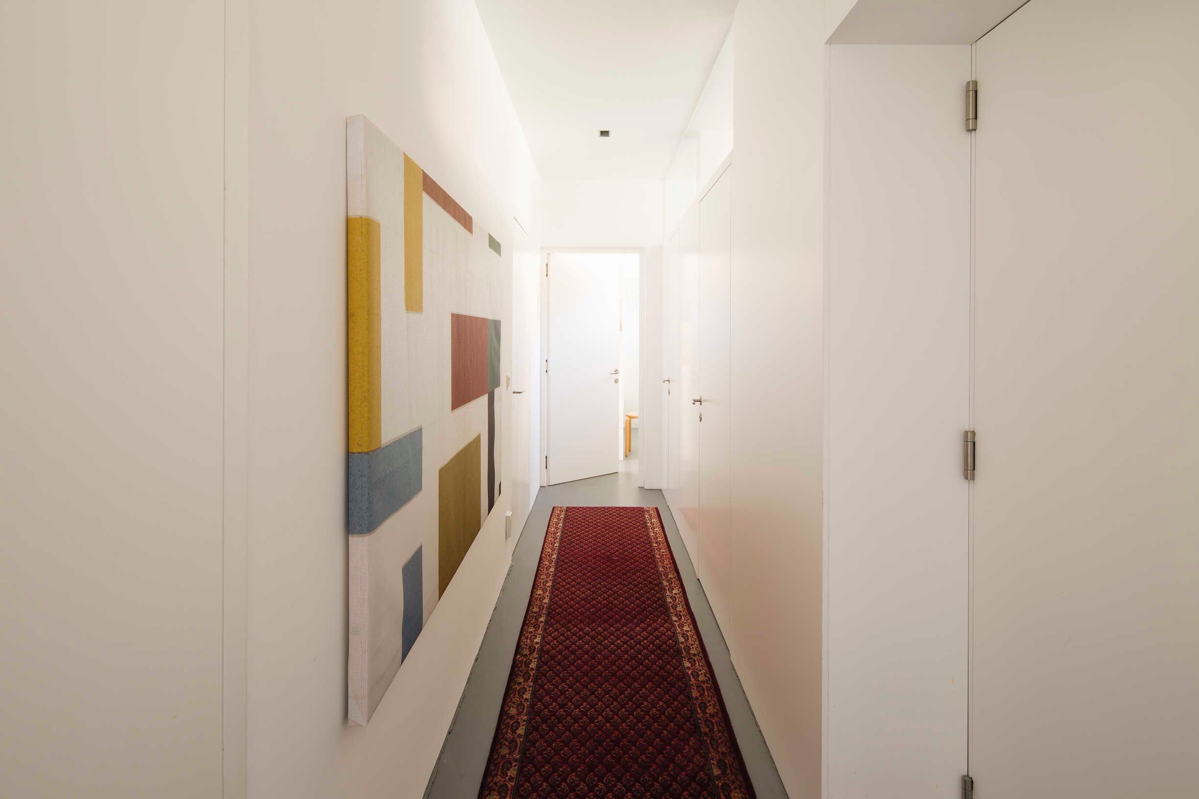 A hallway with a red carpet, white walls, and a door at the end.