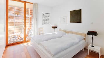 Une chambre à coucher avec un lit, une table de chevet, une lampe, un tableau encadré et une fenêtre avec des stores.