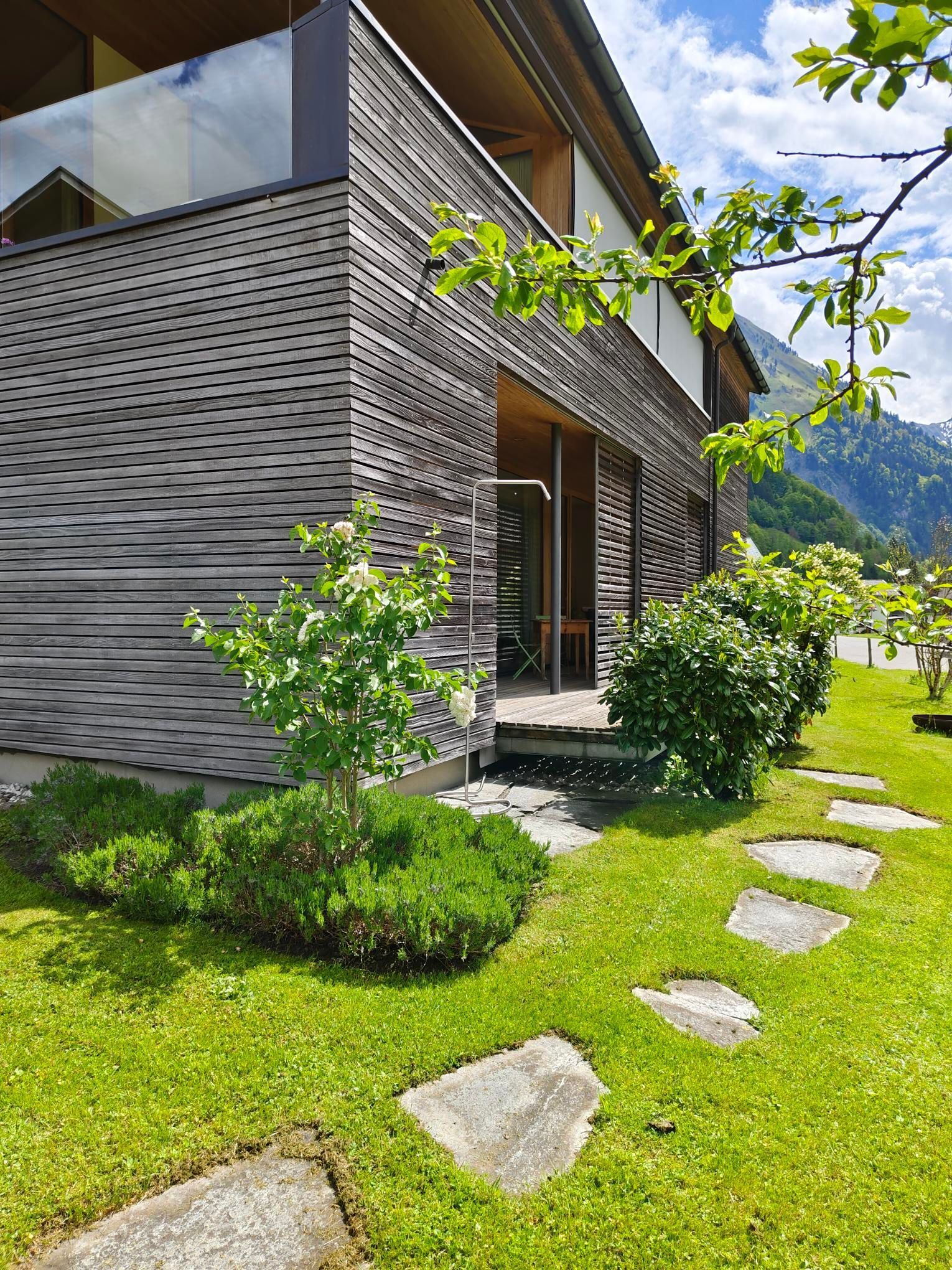A modern house with a wooden exterior, a stone pathway, and lush greenery.