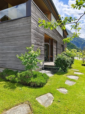 Een modern huis met een houten gevel, een pad van stenen en weelderige begroeiing.