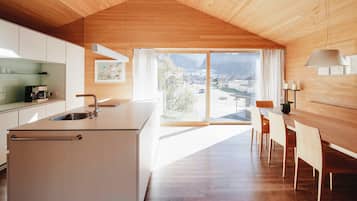 A modern kitchen with a large island, a dining area with wooden chairs, and a view of a town through large windows.