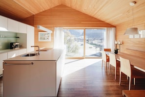 Een moderne keuken met een groot eiland, een eethoek met houten stoelen en uitzicht op een stad door grote ramen.
