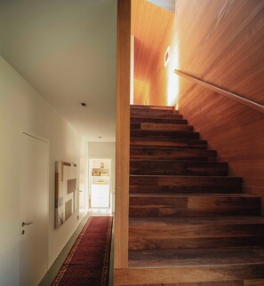 Un escalier en bois mène à une pièce lumineuse, dont la porte se trouve en haut.