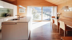 Une cuisine moderne dotée d’un grand îlot central, d’un coin repas avec des chaises en bois et d’une vue sur la ville grâce à de grandes fenêtres.