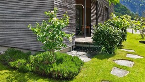 Une maison moderne avec une façade en bois, un chemin en pierre et une végétation luxuriante.