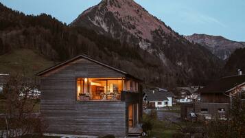 A wooden cabin with a balcony, surrounded by a mountainous landscape.