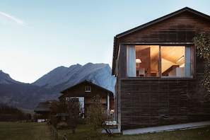 Een modern houten huis met een groot raam, een trap en een berg op de achtergrond.