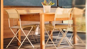 Une table en bois, des chaises et une plante en pot dans un intérieur moderne doté de grandes fenêtres.