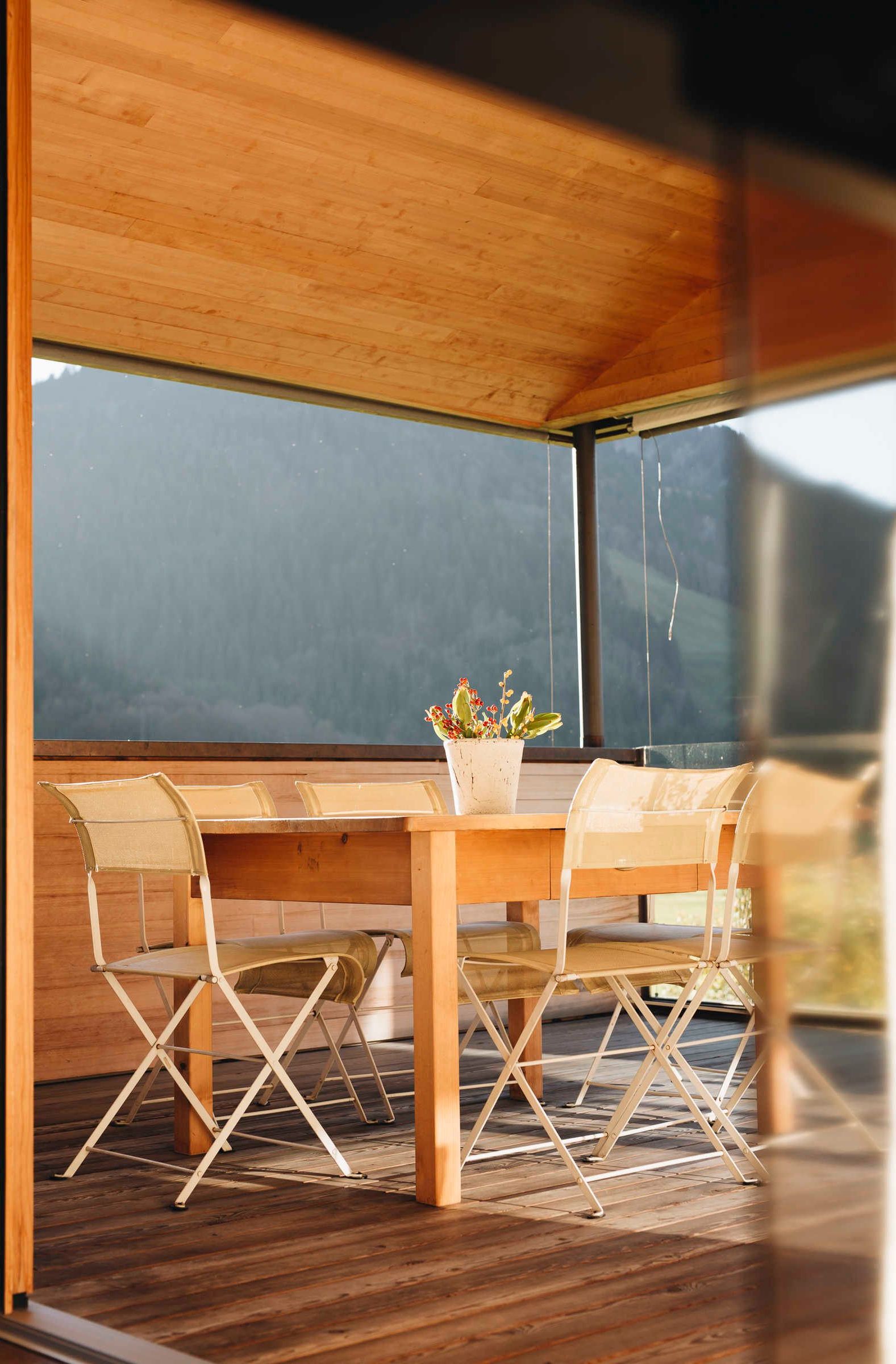 Een houten tafel met stoelen en een plant in pot in een modern interieur met grote ramen.