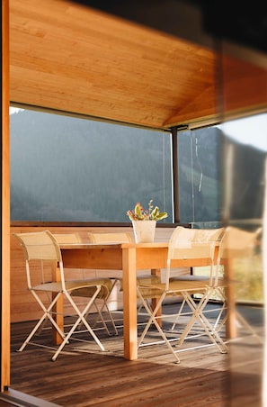 Une table en bois, des chaises et une plante en pot dans un intérieur moderne doté de grandes fenêtres.
