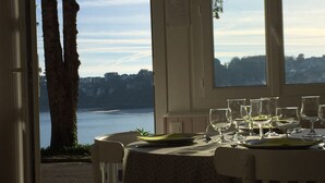 Ein Essbereich im Freien mit Blick auf einen See und Bäume, mit einem Tisch, der mit Weingläsern und Tellern gedeckt ist.