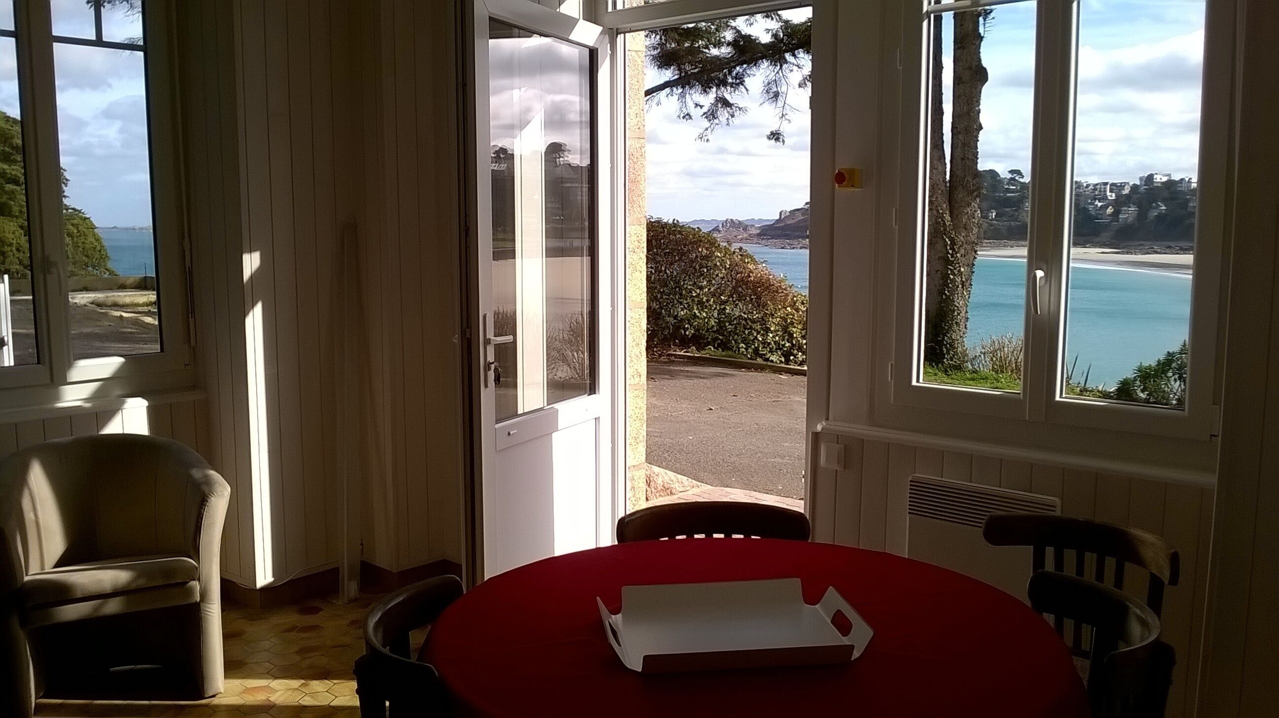 Una habitación con una mesa y sillas, una puerta que da al exterior y vistas al mar y las colinas.